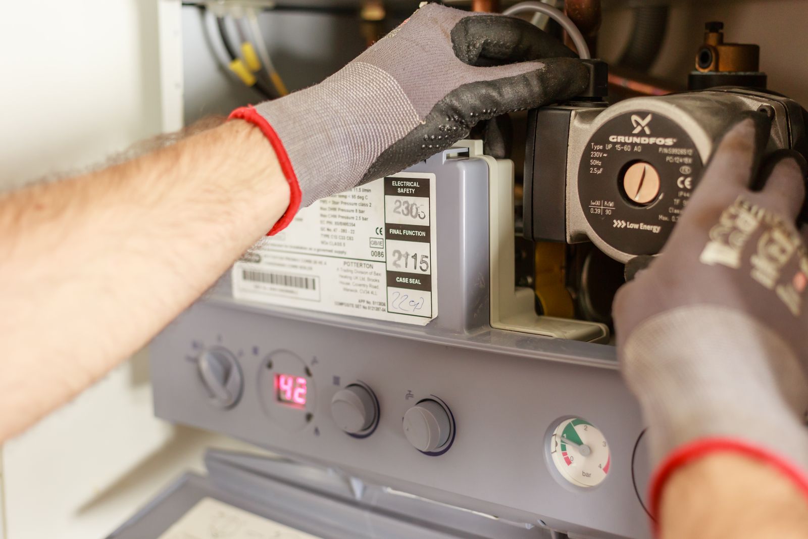 Technician's gloved hands adjusting the control panel of a furnace during a repair