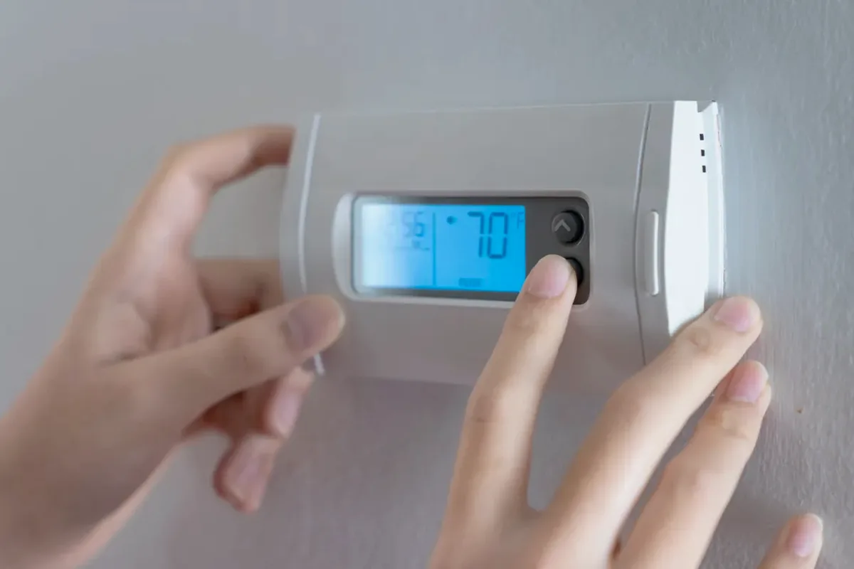 Hands adjusting a digital wall thermostat